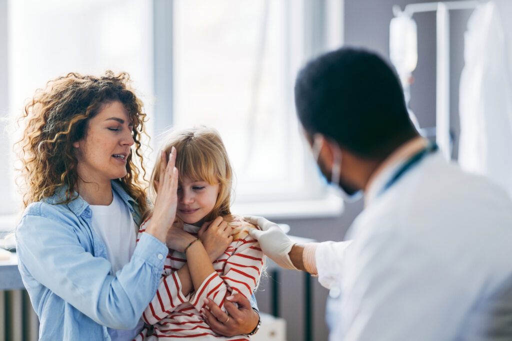 Child being comforted by mother as a doctor examines her after a daycare accident