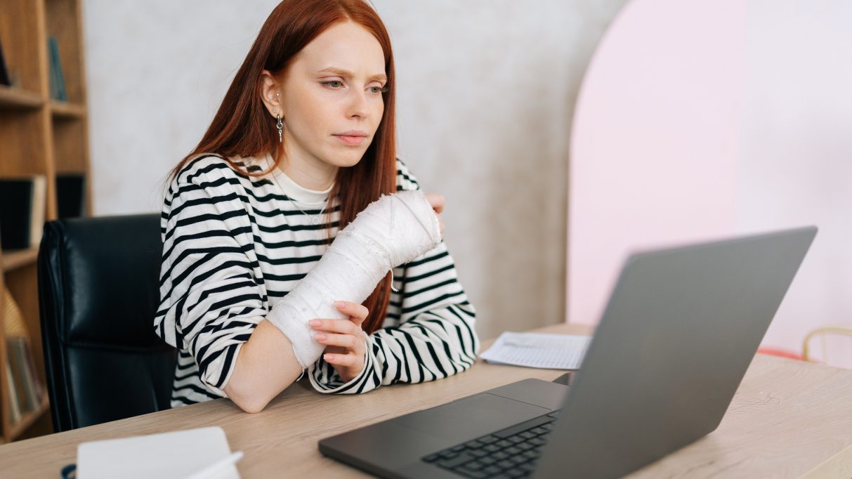 Tired injured young woman with broken right hand wrapped in white gypsum bandage focused looking on laptop computer screen sitting at table. 5 Mistakes to Avoid for Your Injury Claim | Boise Injury Lawyer